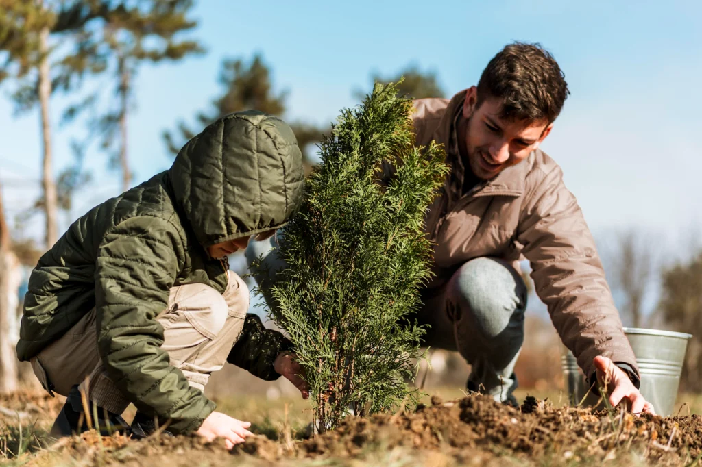 Young volunteer kneeling to plant green seedling in soil alongside mentor in outdoor volunteer activity