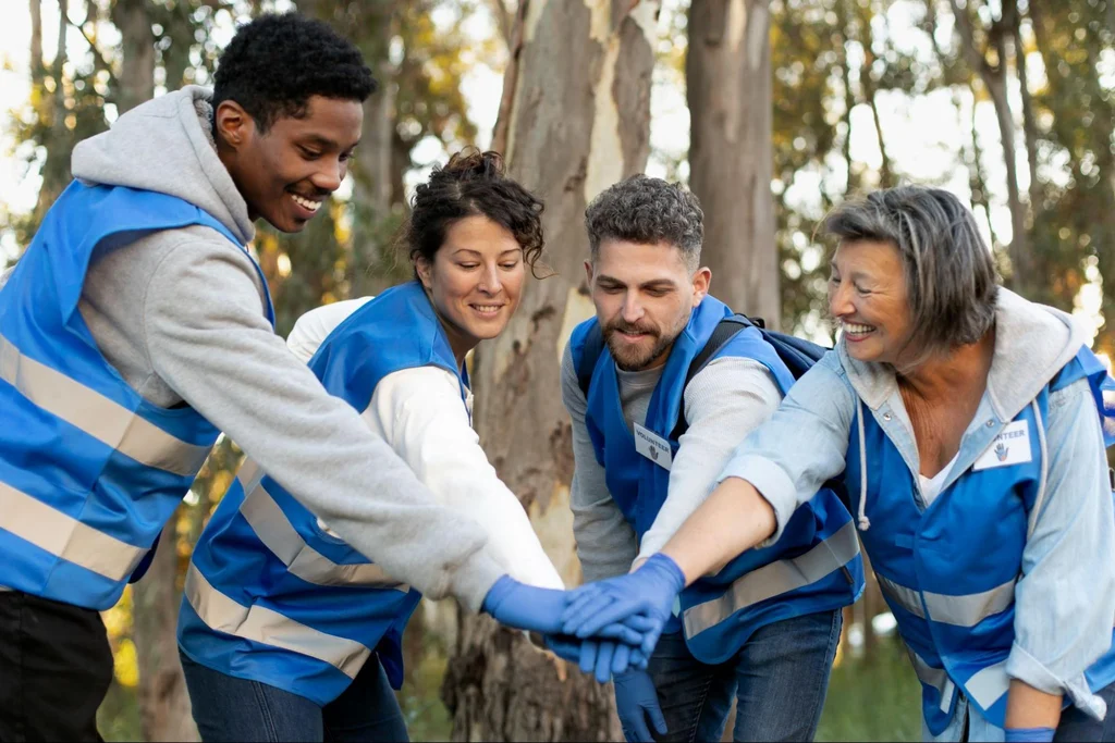 Volunteers in blue vests joining hands in unity gesture during outdoor environmental service project